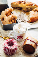 Christmas cookied and cakes with a mugs full of marshmallows, preparation of cokies and cakes for christmas, arranged on a tabletop with christmas decoration