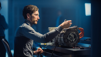 Professional Automotive Engineer in Glasses and Inspection Tools is Testing an Used Electric Engine...
