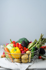 Fresh vegetables in a metal basket on the table. Cherry tomatoes, asparagus, broccoli, potato, peppers, radish, eggplants, zucchini, carrots and onions.
