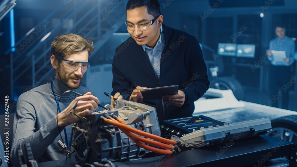 Fototapete Two Professional Automotive Engineers with a Tablet Computer and Inspection Tools are Having a Conversation While Testing an Electric Engine in a High Tech Laboratory with a Concept Car Chassis.