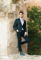 Obraz premium Sexy groom waiting for the bride on the background of beautiful architecture. Rich groom on the wedding day. Elegant groom in a black suit . Wedding day