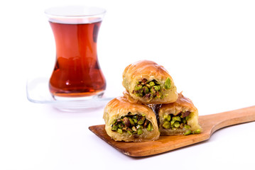 Traditional Turkish Dessert, Baklava on the wooden plate with pistachio nuts and Turkish Tea with spoon on the white surface.