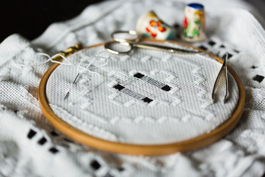 Handmade hemstitch embroidery called Hardanger on wooden hoop, metall scissors, tweezers, needle and thimbles