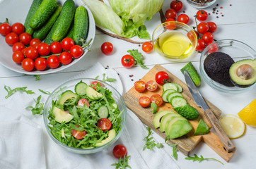 Fresh salad with cucumbers, cherry tomatoes, arugula, avocado, baby corn on white background. Vegetables on wood. Bio Healthy food, herbs and spices. Organic vegetables on wood.