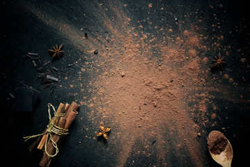 Cocoa powder, sprinkled on a black baking sheet, decorated with cinnamon sticks, star anise and...
