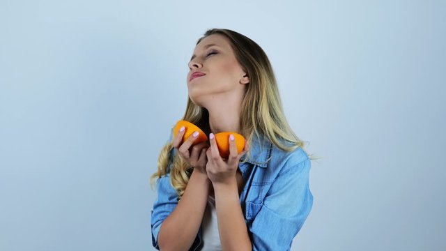 young beautiful blonde woman holding two halves of orange on isolated white background