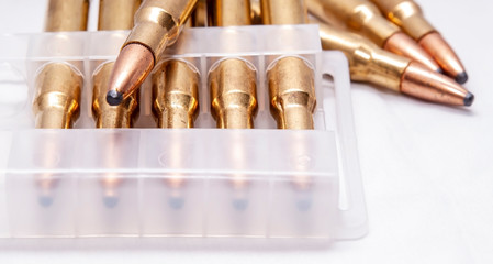 A close up of brass rifle bullets used for hunting, some in a plastic case on a white background