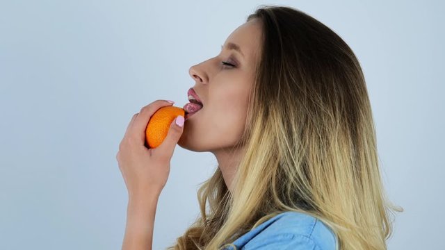 young beautiful sexy blonde woman licks half of fresh orange smiling on isolated white background