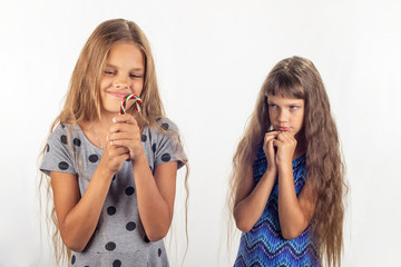 One girl has a lollipop in her hands, the other behind her looks at the girl reproachfully
