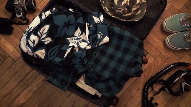 Man hands are fast packing suitcase for a journey. Man dreams about travell. Summer clothing and pasport with money. Top view