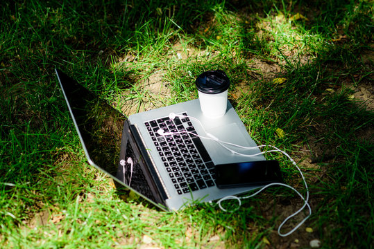 Notebook With Headset Of Mobile Phone And Coffee To Go On Green Grass. Summer Vibes. Relax. University Students Life. Online Shopping. Agile Business. Online Study. Working Place Outdoor. Free Music