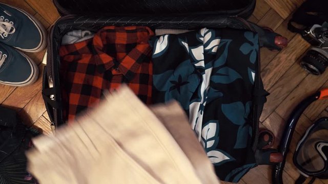 Man hands are fast packing suitcase for a journey. Man dreams about travell. Summer clothing and pasport with money. Top view