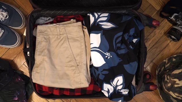 Man hands are packing suitcase for a journey. Man dreams about travell. Summer clothing, pasport with money and diving mask with snorkel. Top view