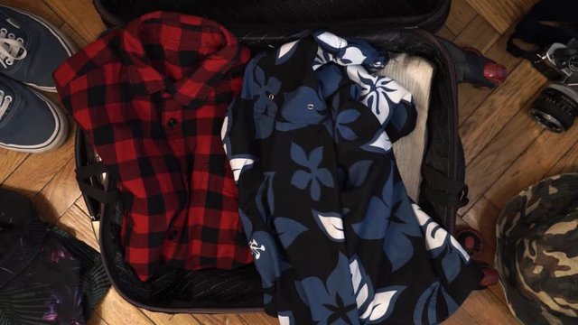 Man hands are fast packing suitcase for a journey. Man dreams about travell. Summer clothing, pasport with money and diving mask with snorkel. Top view