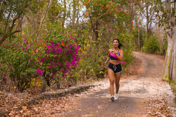 young happy attractive and exotic Asian Indonesian runner woman in jogging workout outdoors at countryside road track nature background running cheerful
