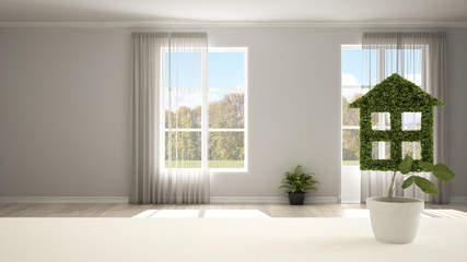 White table top or shelf with green plant in pot shaped like house, empty room with panoramic windows in the background, interior design, real estate, eco architecture concept idea