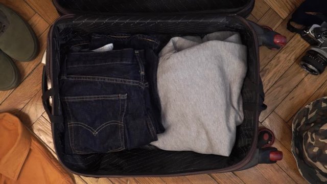 Man hands are fast packing suitcase for a journey. Man dreams about travell. Summer clothing, pasport with money and diving mask with snorkel. Top view