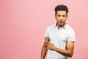 Portrait of happy young good-looking tan-skinned male student with afro hairstyle in casual smiling, pointing aside with finger, looking in camera with excited face expression