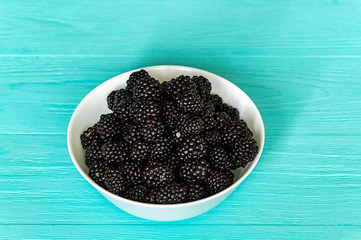 white plate with blackberries, top view in front on a blue wooden background, plate full year concept of healthy food and organic products