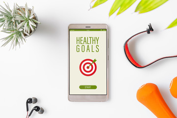 Healthy Goals concept. Fitness healthy goals with mockup mobile phone on white table with dumbbells,smart watch, earphone. Mock up smartphone for fitness healthy concept.