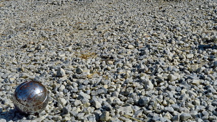 Gros plan sur une boule de pétanque usée sur terrain de gravier.