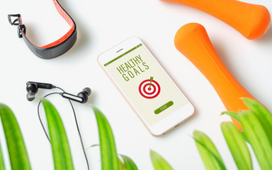 Healthy Goals concept. Fitness healthy goals with mockup mobile phone on white table with dumbbells,smart watch, earphone. Mock up smartphone for fitness healthy concept.