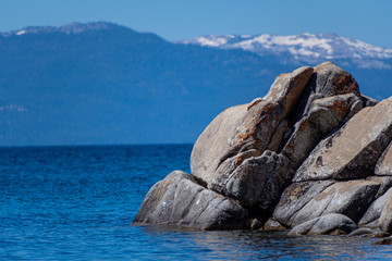A Granite Boulder Sitting In A Large Lake Surrounded by Snowy Mountains