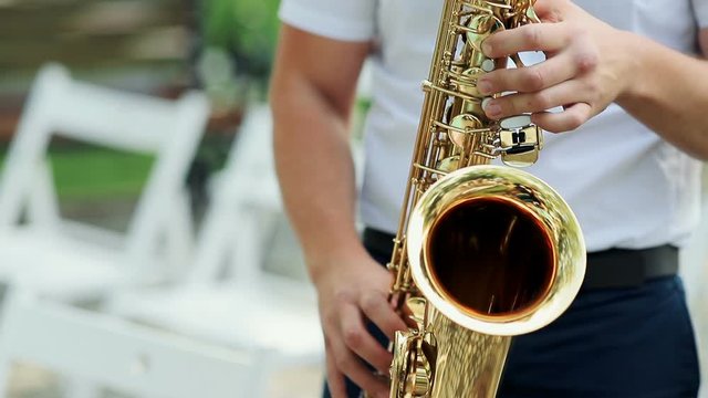 Closeup, of male's hands playing the saxophone outdoors.