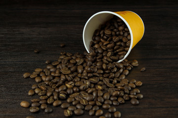 Scattered coffee beans and coffee cup on a wooden board, close-up. Design concept.