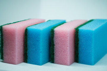 Different color sponges for washing dishes, staggered on top of each other close up on a white background