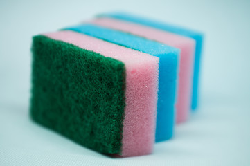 Different color sponges for washing dishes, staggered on top of each other close up on a white background