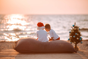 Two little boys on the beach at Christmas with a New Year tree.