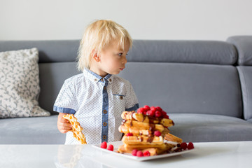 Sweet toddler birthday boy, eating belgian waffle with raspberries and chocolate