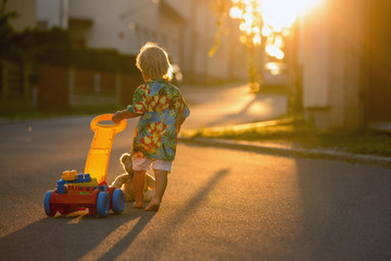 Beautiful toddler child, playing with plastic toys, blocks, cars on sunset