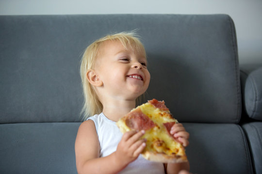 Cute little Caucasian kid eating pizza. Hungry child taking a bite from pizza on a pizza party, outdoors