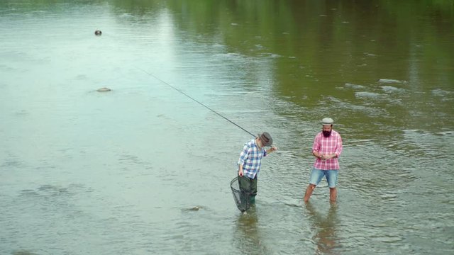 Father and son ishing. Fly fisherman using fly fishing rod in beautiful river. Family and generation - summer holidays and people concept. Man fishing and relaxing while enjoying hobby.