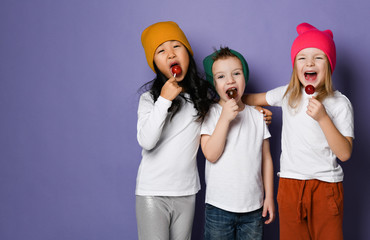 Three kids happy friends boy and two girls in white t-shirts, colorful pants and hats hugging and...