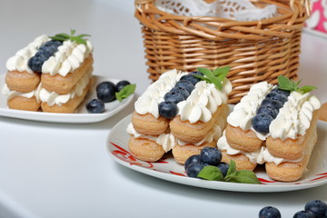 Cakes made from Italian savoyardi cookies and cream. Decorated with blueberries and mint leaves. Fresh blueberries are collected in a wicker basket.