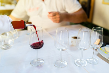 Man sommelier waiter pouring wine in the drinking glass at the testing ceremony event for the expert to test it and give marks about the quality to the degustation card
