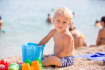 Beautiful two years old toddler child, boy, playing with beach toys on the beach coast near water
