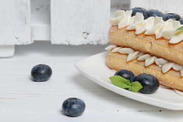 Cakes made from Italian savoyardi cookies and cream. Decorated with blueberries and mint leaves. Nearby is a box of white painted wooden boards.