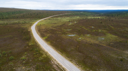  Aerial view of the road and taiga fields in summer on a cloudy day. Abstract landscape of northern nature with drone. 