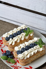 Cakes made from Italian savoyardi cookies and cream. Decorated with blueberries and mint leaves. Nearby is a box of white painted wooden boards.