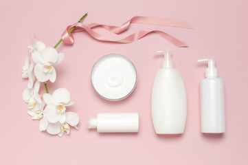 Beauty Spa concept. Opened container with cream, cosmetic bottle containers, white Phalaenopsis orchid flowers on pink background Flat lay top view. Herbal dermatology cosmetic hygienic cream
