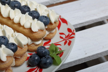 Cakes made from Italian savoyardi cookies and cream. Decorated with blueberries and mint leaves. They stand on a box of white painted wooden boards.