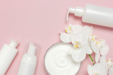 Obraz na płótnie Canvas Beauty Spa concept. Opened container with cream, cosmetic bottle containers, white Phalaenopsis orchid flowers on pink background Flat lay top view. Herbal dermatology cosmetic hygienic cream