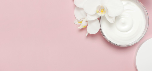 Beauty Spa concept. Opened plastic container with cream and White Phalaenopsis orchid flowers on pink background Flat lay top view. Herbal dermatology cosmetic hygienic cream, organic cosmetic Natural