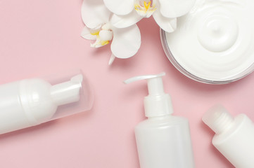 Beauty Spa concept. Opened container with cream, cosmetic bottle containers, white Phalaenopsis orchid flowers on pink background Flat lay top view. Herbal dermatology cosmetic hygienic cream
