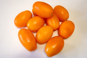 Pile of orange plum tomatoes on white fabric background