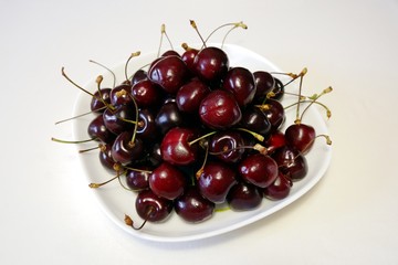 Obraz na płótnie Canvas Ripe dark red cherries on white square plate